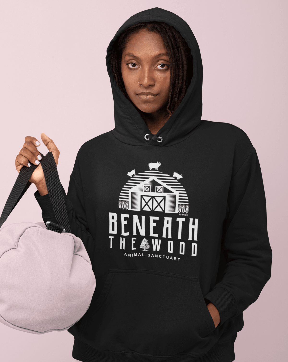 Person wearing a black hoodie with 'Beneath the Wood Animal Sanctuary' design on a pink background (gender-women)