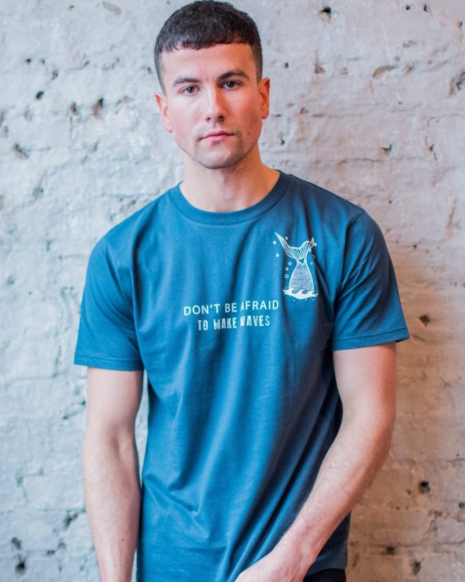 Male model posing against a brick wall wearing a denim blue t-shirt with marine themed design on the front. Designed by eco-ethical award winning Viva La Vegan.
