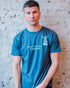 Male model posing against a brick wall wearing a denim blue t-shirt with marine themed design on the front. Designed by eco-ethical award winning Viva La Vegan.