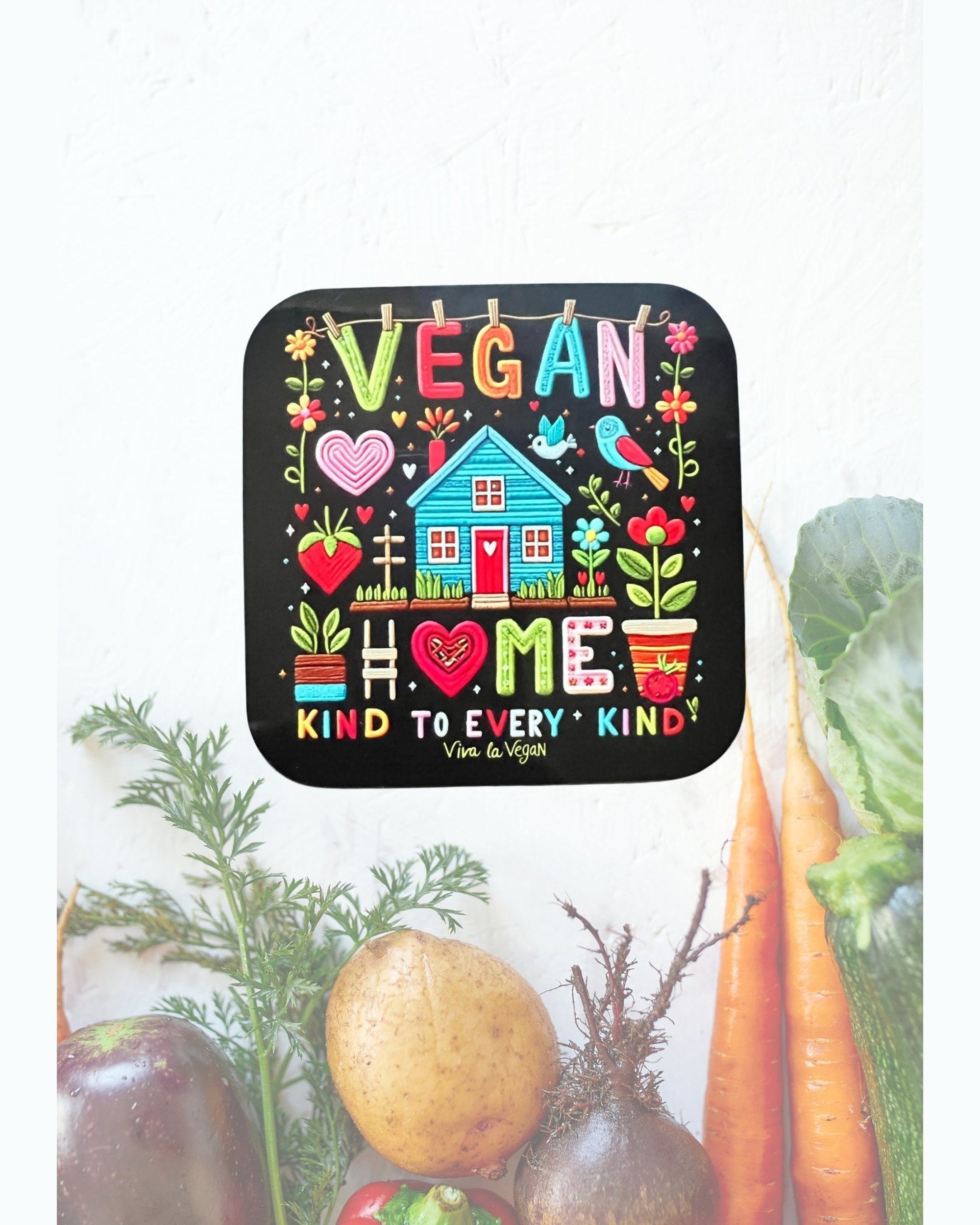 Vegan statement coaster with the wording Vegan Home a picture of a brightly coloured house in the style of embroidery. Black background with a colourful design