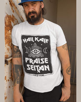 Bearded man in cap wearing a white organic Vegan T-shirt with a bold Hail Kale Praise Seitan statement printed on it. The design is by eco ethical brand Viva La Vegan
