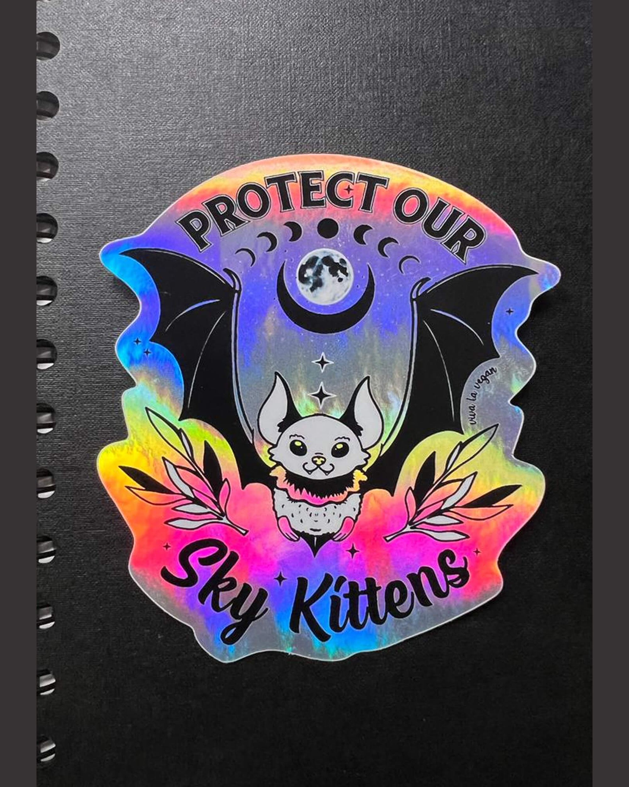 Sky Kittens holographic sticker on a black note book. by eco ethical brand Viva La Vegan